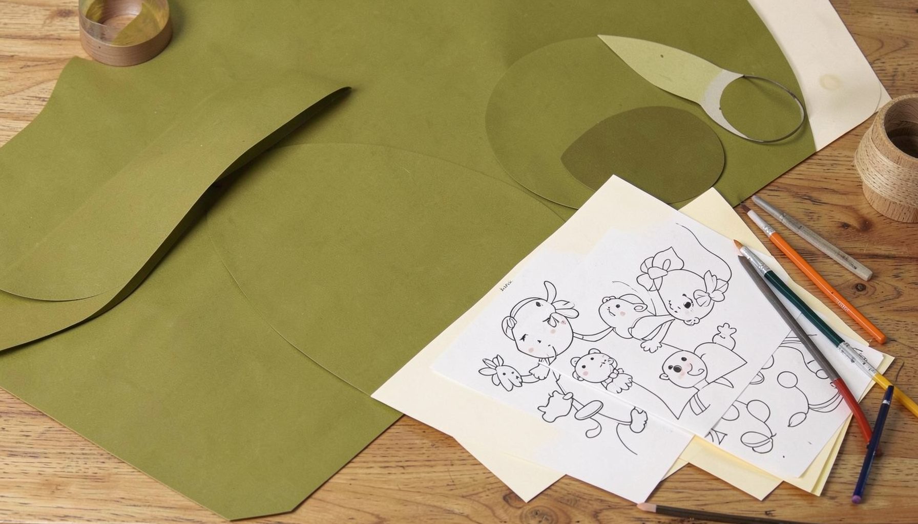 A warm olive-green and cream abstract composition of art supplies and printed coloring sheets on a wooden table, calm and creative atmosphere